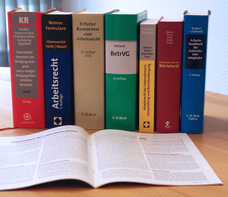 juristische Bücher stehen nebeneinander auf einem Tisch; davor aufgeblättert ein Kommentar-Heft